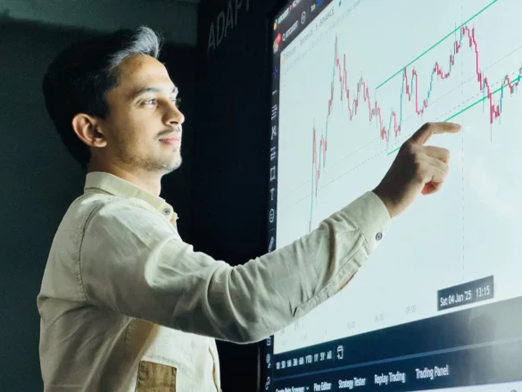 Man in a light shirt pointing at a large trading chart projected on a screen.