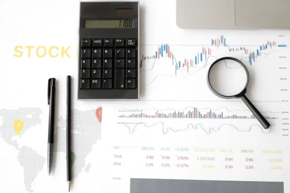 Desk with stock charts, a magnifying glass, calculator, and pens; symbolizes financial analysis.